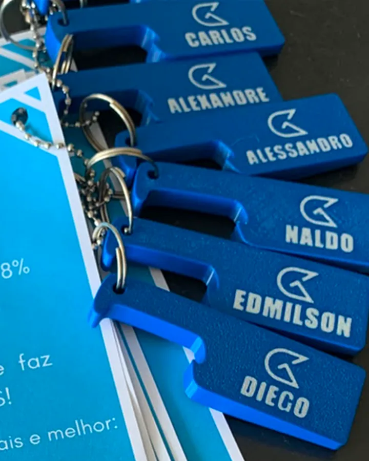 Conjunto de chaveiros impressos em 3D, cada um com o nome de uma pessoa e a marca da empresa